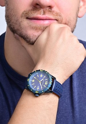 Watch with a dark blue silicone strap, black case, and blue dial featuring yellow accents, large numbers, and a date display.