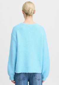 Maglione oversize di colore azzurro chiaro, lavorato a maglia, con orlo a costine e maniche larghe. Realizzato in un morbido tessuto testurizzato. Indossato sopra dei jeans blu.