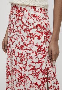 Gonna floreale con una base bianca e motivi astratti rossi, tessuto testurizzato, spacco laterale e dettagli con bottoni sulla cucitura.