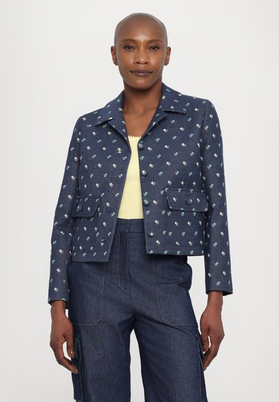 Jachetă din denim cu un model floral, de culoare albastră închisă, cu guler, două buzunare frontale și închidere cu nasturi. Stilizată cu un top de culoare galben deschis.