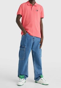 Rosa pikétröja med krage, kombinerad med lösa blå denim cargo-byxor med sidofickor, och vita sneakers med gröna detaljer.