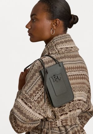 Green leather handbag with embossed logo, rectangular shape, and adjustable strap. Worn over a patterned brown knit coat.