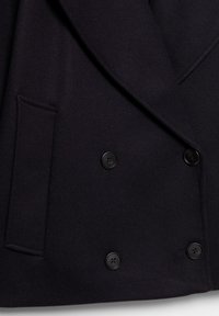 Manteau noir croisé avec quatre boutons noirs, col à revers cranté et une poche à rabat horizontale sur le côté gauche.