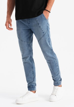 Pantalons de jogging bleu clair avec des poignets élastiques, dotés d'un design à panneaux et de poches, associés à des baskets blanches. Fabriqués en tissu en denim.