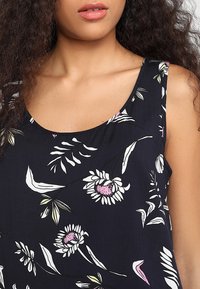 Kwiatowa, bezrękawnikowa bluzka w granatowym kolorze z białymi i różowymi stokrotkami, z zielonymi liśćmi i okrągłym dekoltem. Miękki, lekki materiał.