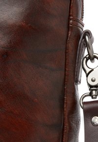 Brown leather bag with a smooth texture, featuring a metal clip attachment and dark stitching details along the edges.