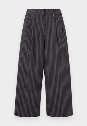 Μαύροι φαρδιά παντελόνια cropped με λευκές κατακόρυφες ρίγες και θηλιές ζώνης σε φωτεινό φόντο.