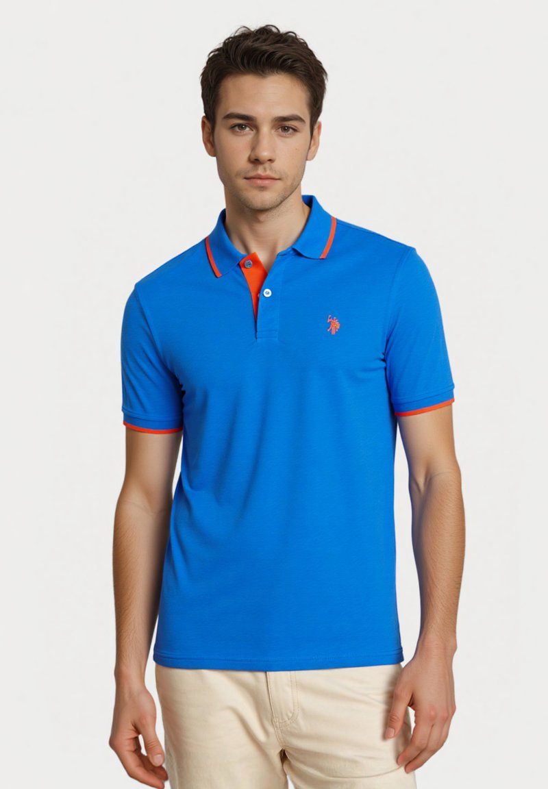 Blå polo t-shirt med orange detaljer ved kraven og ærmerne, med et lille logo på venstre brystområde. Korte ærmer, klassisk pasform.