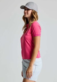 Roze polo shirt met korte mouwen, kraag en knopenlijst, gecombineerd met lichtblauwe shorts. Een grijze pet maakt de sportieve look compleet.