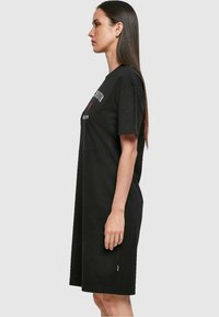 Czarna bawełniana sukienka t-shirt z krótkimi rękawami, luźny krój, okrągły dekolt oraz graficzny nadruk na klatce piersiowej. W średniej długości z bocznymi rozporkami.