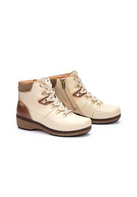 Bottines beiges et marron en cuir, avec fermeture à lacets et zip, semelle texturée et accents contrastants sur le talon.