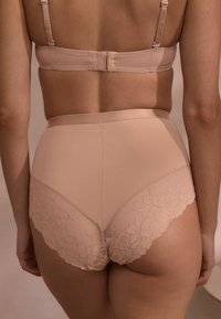 Beige högmidjade underkläder har ett slätt tyg med blommigt spetsdetaljer längs benen, vilket ger en kontrast i textur och design.
