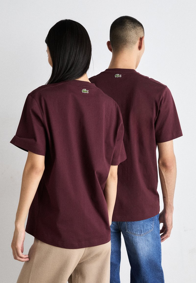 T-shirts en coton bordeaux à manches courtes, avec un petit logo vert au niveau de l'encolure arrière et une coupe décontractée.