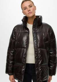 Tumepruun pehme voodriga jope kõrge kraega, millel on läikiv tekstuur, lukuga sulgemine ja kaks esitaskut. Lihtne geomeetriline tikand.