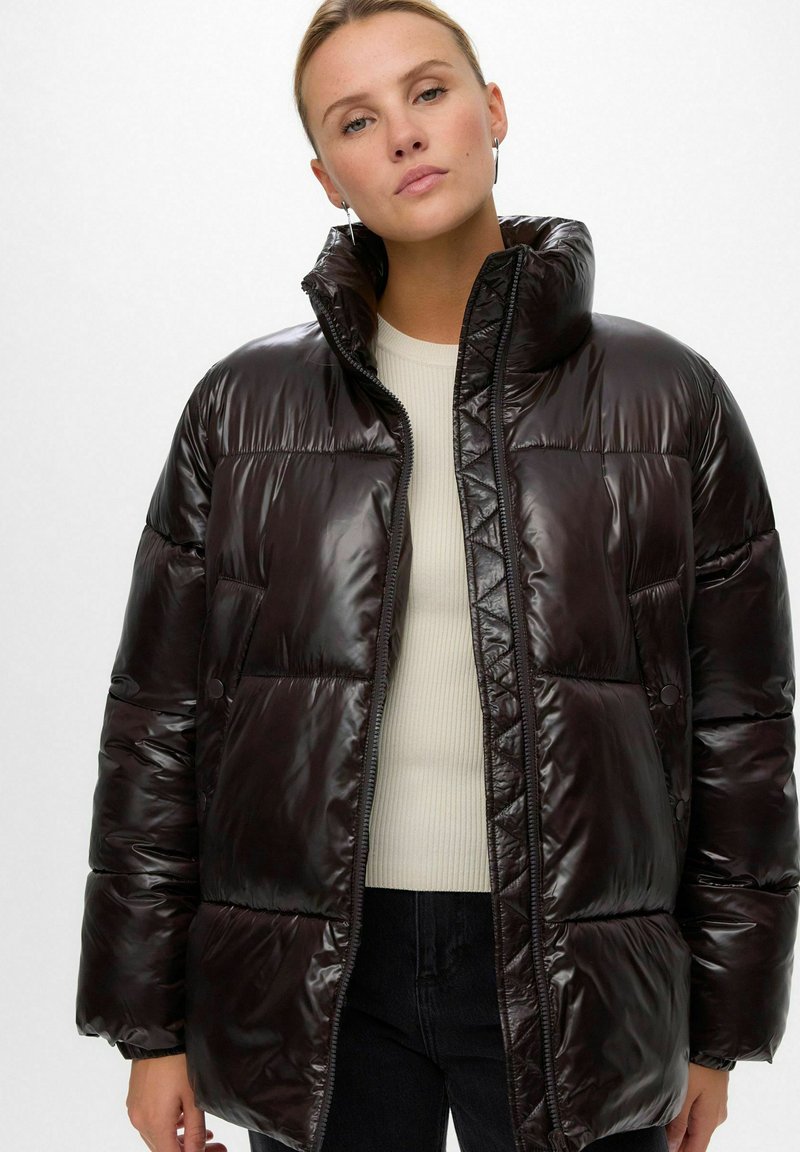 Tumepruun pehme voodriga jope kõrge kraega, millel on läikiv tekstuur, lukuga sulgemine ja kaks esitaskut. Lihtne geomeetriline tikand.