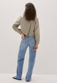 Camicia verde oliva tagliata, con maniche lunghe, abbinata a jeans a vita alta azzurri chiari con due tasche posteriori e gamba dritta.
