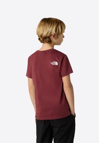 Vinrød bomulds t-shirt med hvidt logo på ryggen, rund hals og korte ærmer. Stoffet virker glat og åndbart.