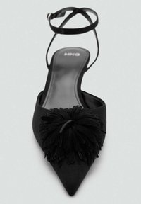 Zapato de ante negro tipo slingback con punta afilada y un gran detalle de borlas en la parte frontal. Correa en el tobillo ajustable para un mejor ajuste.