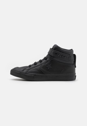 Baskets montantes Converse noires avec logo étoile, fermeture à lacets et bride Velcro, vues de côté sur fond blanc.