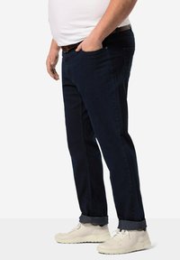 Tummansiniset farkut denimpäällysteessä, suoranlahkeinen malli, jossa on etutaskut ja käärityt lahkeet, yhdistettynä valkoisiin urheilukengiin.