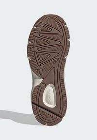 Smeđi gumeni đon tenisica s teksturiranim uzorcima za prianjanje, s glatkim bež dijelom i konstruiranim oblicima za udobnost.