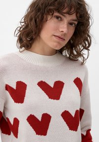 Maglione lavorato a maglia di colore crema con grandi motivi a cuore rosso, collo a girocollo testurizzato e tessuto lavorato in modo morbido.