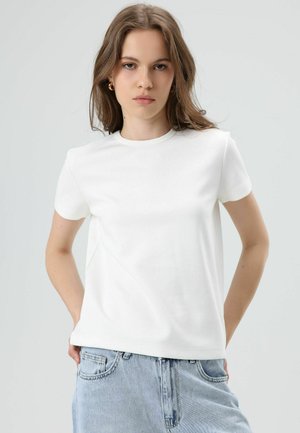 Witte korte mouw t-shirt gemaakt van zachte stof, met een ronde hals en subtiele naaddetails, gecombineerd met lichtblauwe spijkerbroek.