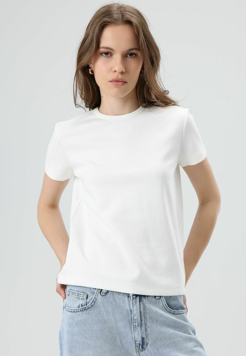 Witte korte mouw t-shirt gemaakt van zachte stof, met een ronde hals en subtiele naaddetails, gecombineerd met lichtblauwe spijkerbroek.