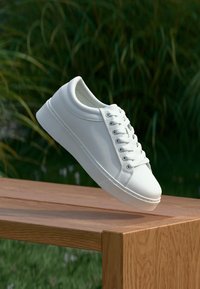 Sneaker bianco con tomaia in morbida pelle, punta rotonda e suola in gomma. Presenta sei occhielli, lacci e sottili dettagli testurizzati sui lati.