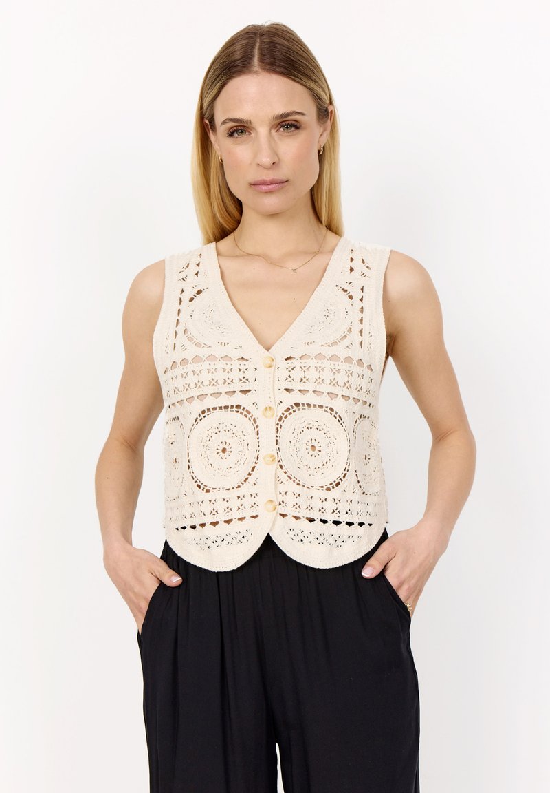 Beige Strickweste mit Lochmustern, V-Ausschnitt und fünf Knöpfen. Mit gewelltem Saum und filigranen kreisförmigen Designs.