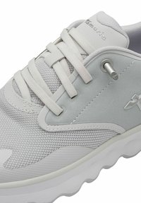 Chaussure de sport gris clair avec une tige en maille, des accents argentés texturés, des lacets plats et une semelle blanche rembourrée avec un motif en vagues.