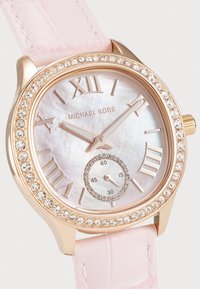 Reloj de pulsera redondo con caja y bisel de oro rosa, correa de cuero con estampado de cocodrilo en color rosa, esfera de madreperla blanca y detalles de cristal.