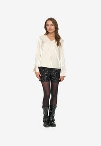 Glossy cream v-neck top with bell sleeves, paired with black sequin shorts and black knee-high boots. Smooth texture and fitted design.