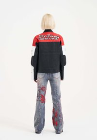Chaqueta de motocicleta de cuero negro con acentos en rojo y blanco, que presenta texto bordado. Jeans de denim de cintura alta con patrones de bordado en rojo.