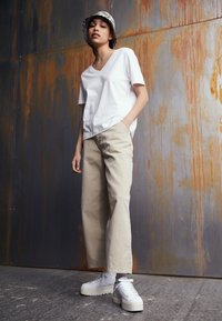 Vit kortärmad V-ringad t-shirt, beige vida byxor och vita plattformssneakers. Svart- och vitmönstrad bucket hat. Textur färg.