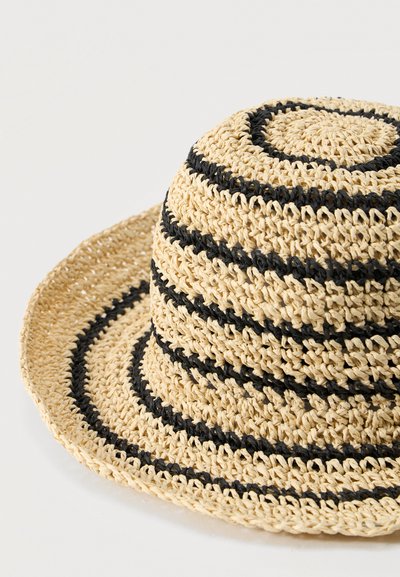 Μπεζ πλεκτό ψάθινο καπέλο με μαύρες οριζόντιες ρίγες και φαρδύ γείσο, απεικονίζεται πάνω σε απλό φωτεινό φόντο.