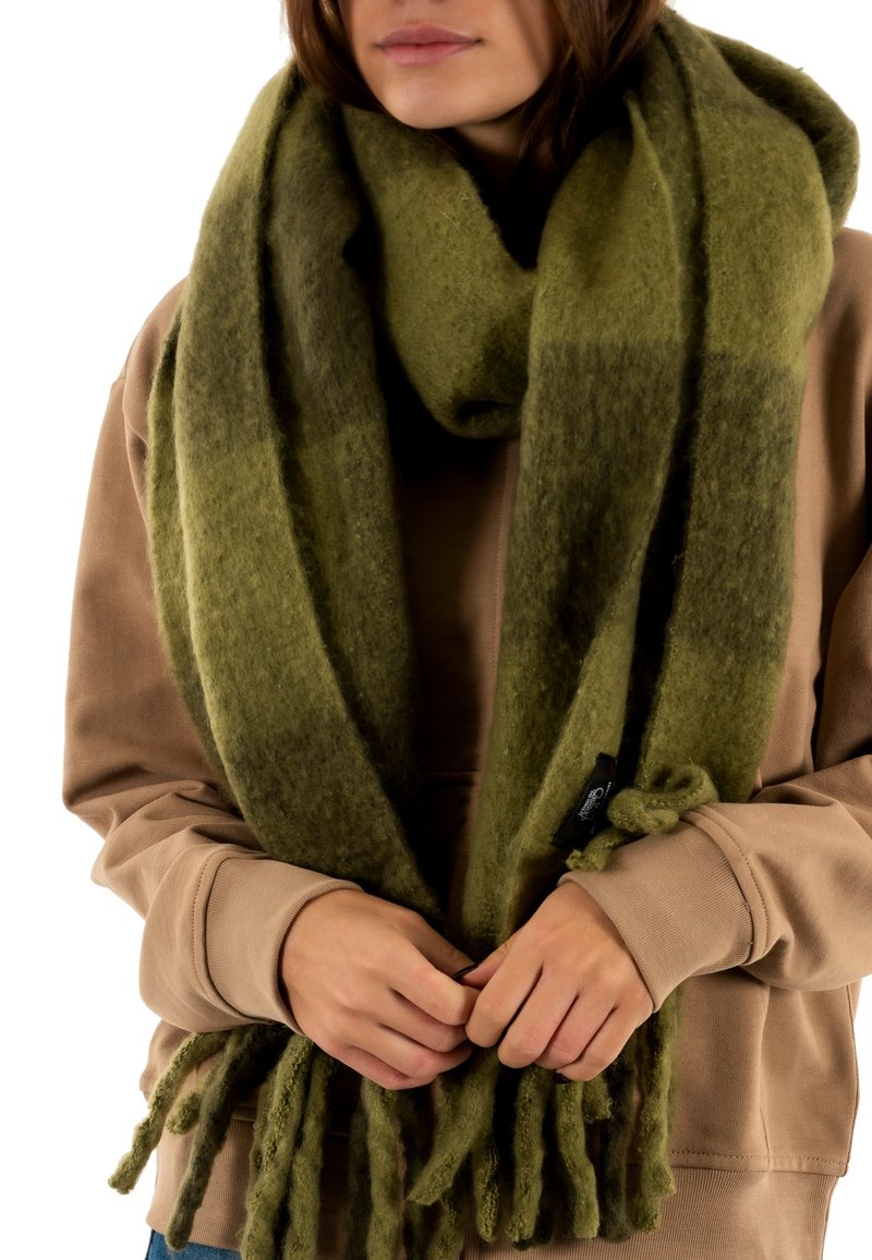 Scarf di lana verde spessa con tonalità più scure alle estremità, dotato di bordi frangiati e una finitura morbida e testurizzata. Si drappeggia attorno al collo.