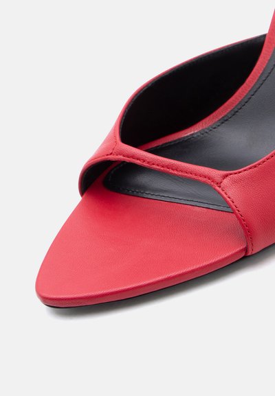 Κόκκινο δερμάτινο mule με ανοιχτά δάχτυλα, μαύρη εσωτερική σόλα και έναν απλό ιμάντα μπροστά σε λευκό φόντο.