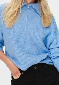 Suéter de punto azul claro con cuello con cremallera y patrón texturizado. Tela suave, corte holgado, con dobladillo redondeado y puños acanalados.