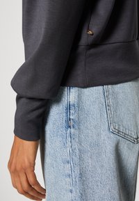 Donkergrijze sweatshirt met een soepele textuur, voorzien van een zijknopdetail, gecombineerd met lichtblauwe jeans in een vervaagde wassing en rechte snit.