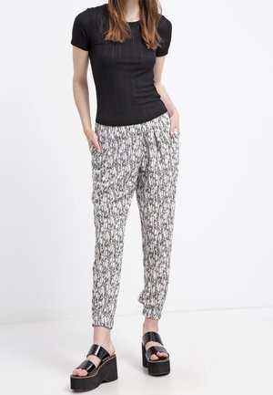 Haut noir à manches courtes côtelées associé à un pantalon blanc à motifs avec un design de feuilles et des poignets élastiques. Porté avec des sandales à plateforme noires.