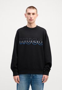 Felpa nera con collo a giro, caratterizzata da una scritta "HUGO" bold in gradiente blu. Maniche lunghe e polsini a costine completano il design.