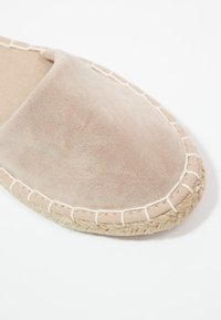 Espadrille en daim beige avec couture blanche et semelle en jute, montrant un gros plan de la zone de l'orteil arrondi.