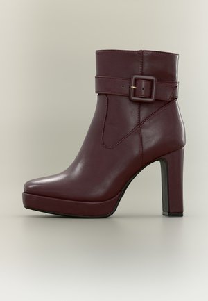 Bottine en cuir marron foncé avec talon bloc haut, semelle plateforme et bride décorative à boucle autour de la cheville.