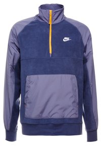Nike-pullover i nyanser av mörkblått och grått, med fleece-material, kvartszipp, orange dragkedjedetalj och framficka.