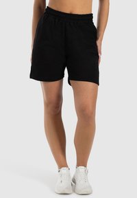 Zwarte katoenen shorts met een elastische tailleband, voorzien van zijzakken en een subtiele logodetail. Gemaakt in combinatie met witte sportieve schoenen.