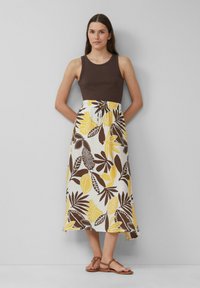 Bruine tanktop gecombineerd met een middellange rok met gele en bruine bladmotieven op een witte achtergrond. Bruine sandalen met bandjes.