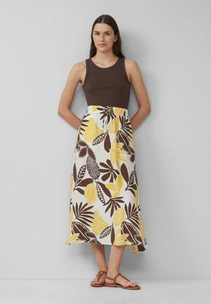 Bruine tanktop gecombineerd met een middellange rok met gele en bruine bladmotieven op een witte achtergrond. Bruine sandalen met bandjes.