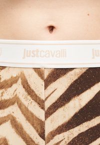 Κοντινό πλάνο της μέσης με κολάν σε ζωικό μοτίβο και λευκή ελαστική μέση με το λογότυπο "Just Cavalli".