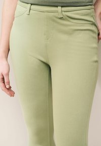 Grüne Stretch-Hosen mit schlanker Passform, die eine glatte Textur, Fronttaschen und einen schlichten Bund aufweisen, geeignet für die Freizeit.